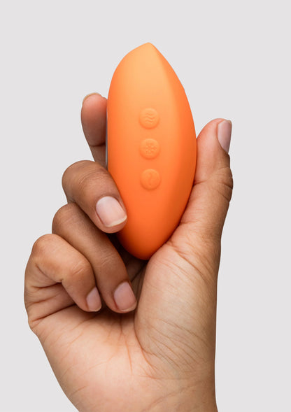 Oranje Temp massager met reliëfknoppen aan de onderkant, vastgehouden in hand