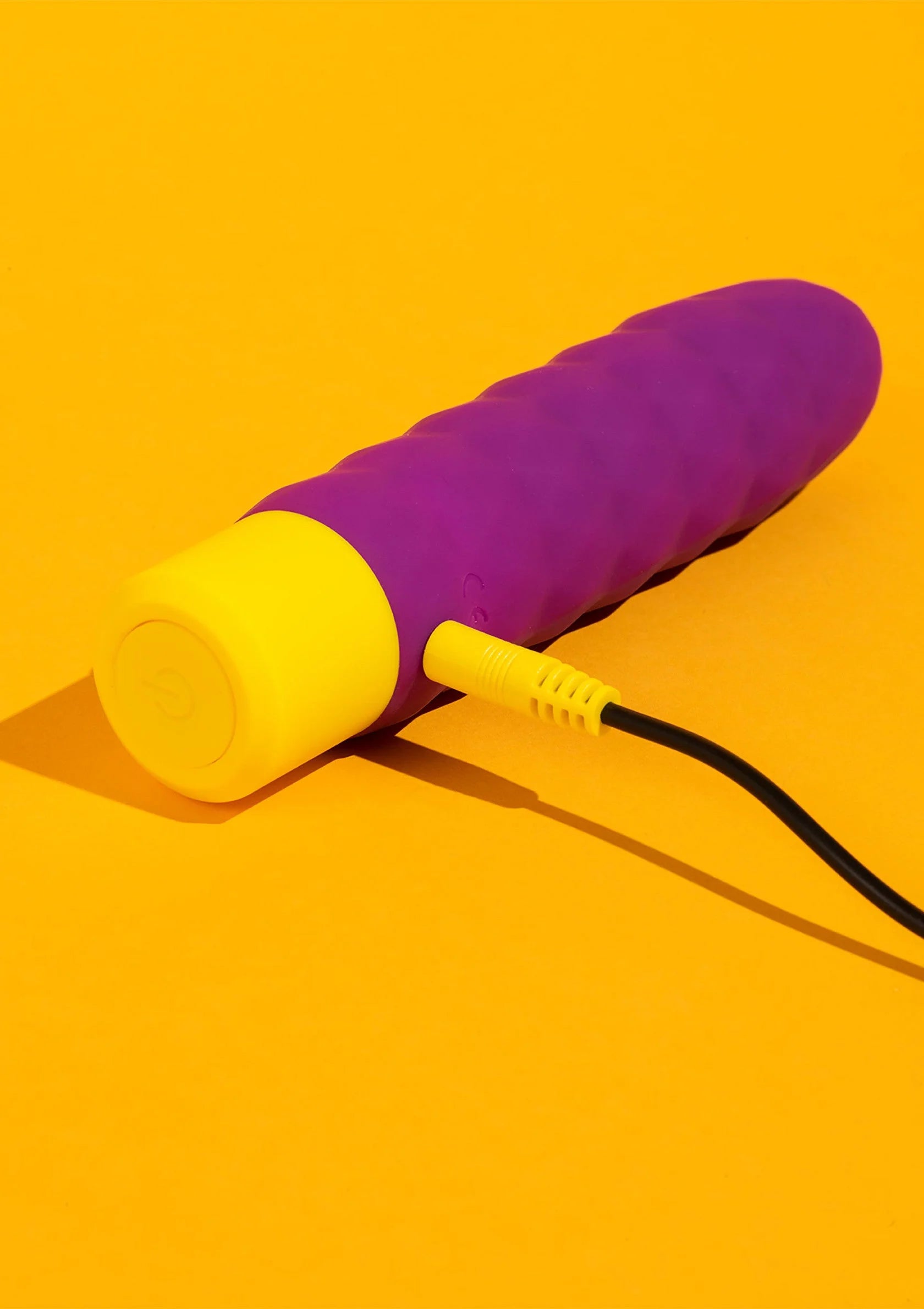 Paarse vibratiestaaf opzij met gele basis en zwarte oplaadkabel.
