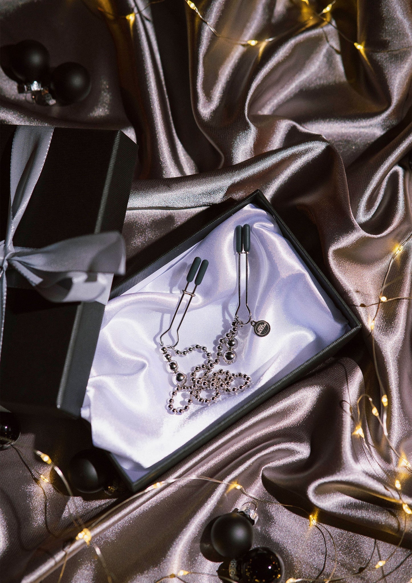 Tepelknijpers met zilverkleurige kralenketting en metalen klemmen op satijn
