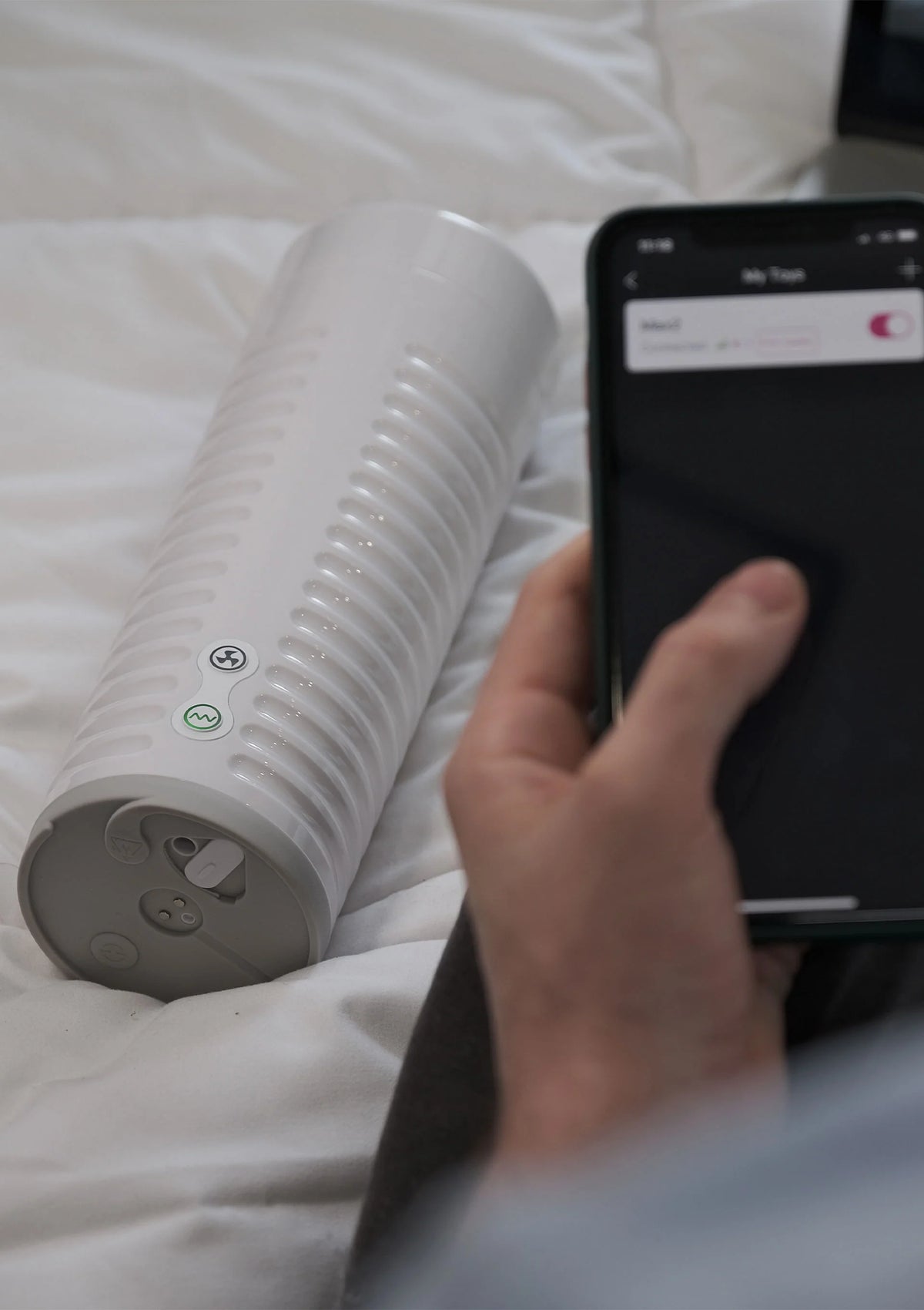 Wit ribbelcilinder stimulatieapparaat op bed met smartphone in beeld