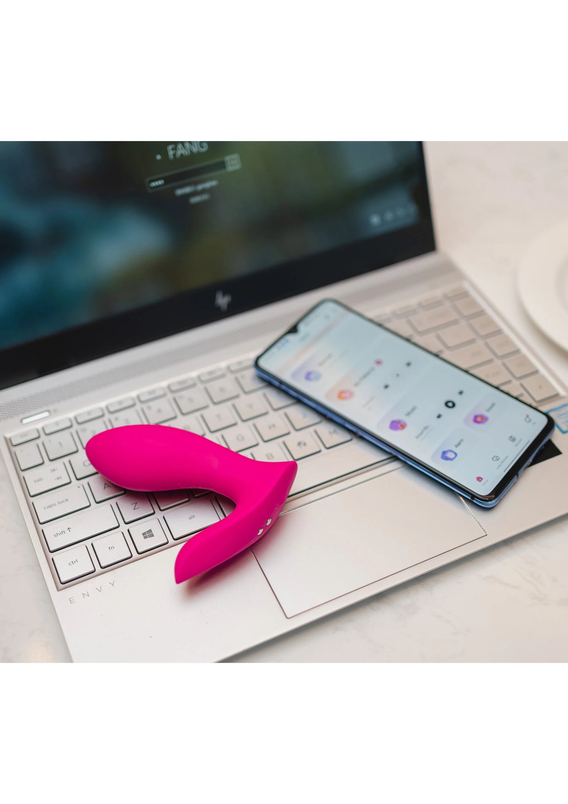 Roze koppelvibrator naast smartphonebediening op een laptop