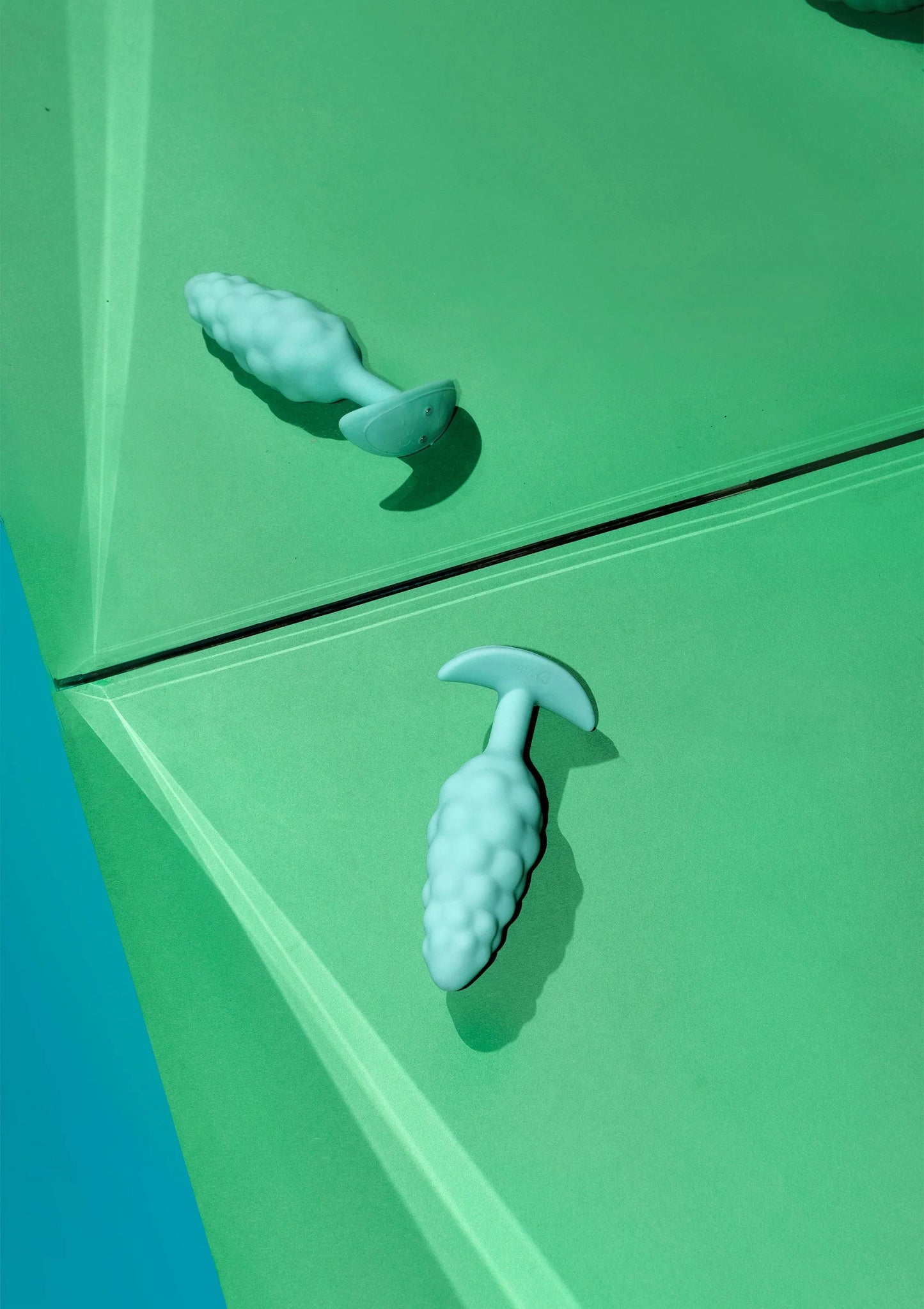 Turquoise anale plug met bultenstructuur en brede voet, deels zichtbaar