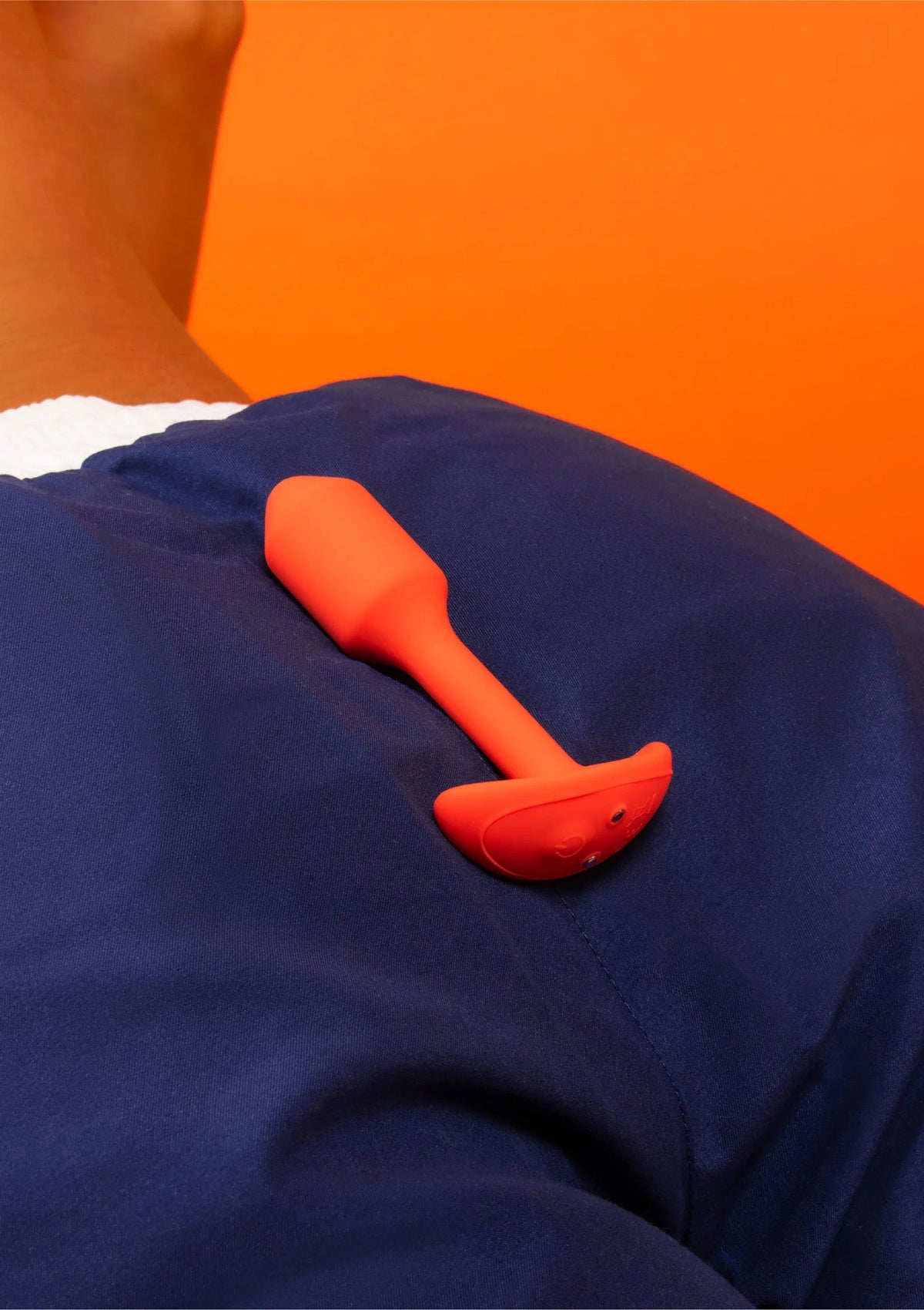 Trillende snug plug van B-Vibe, oranje plug op donkerblauwe stof