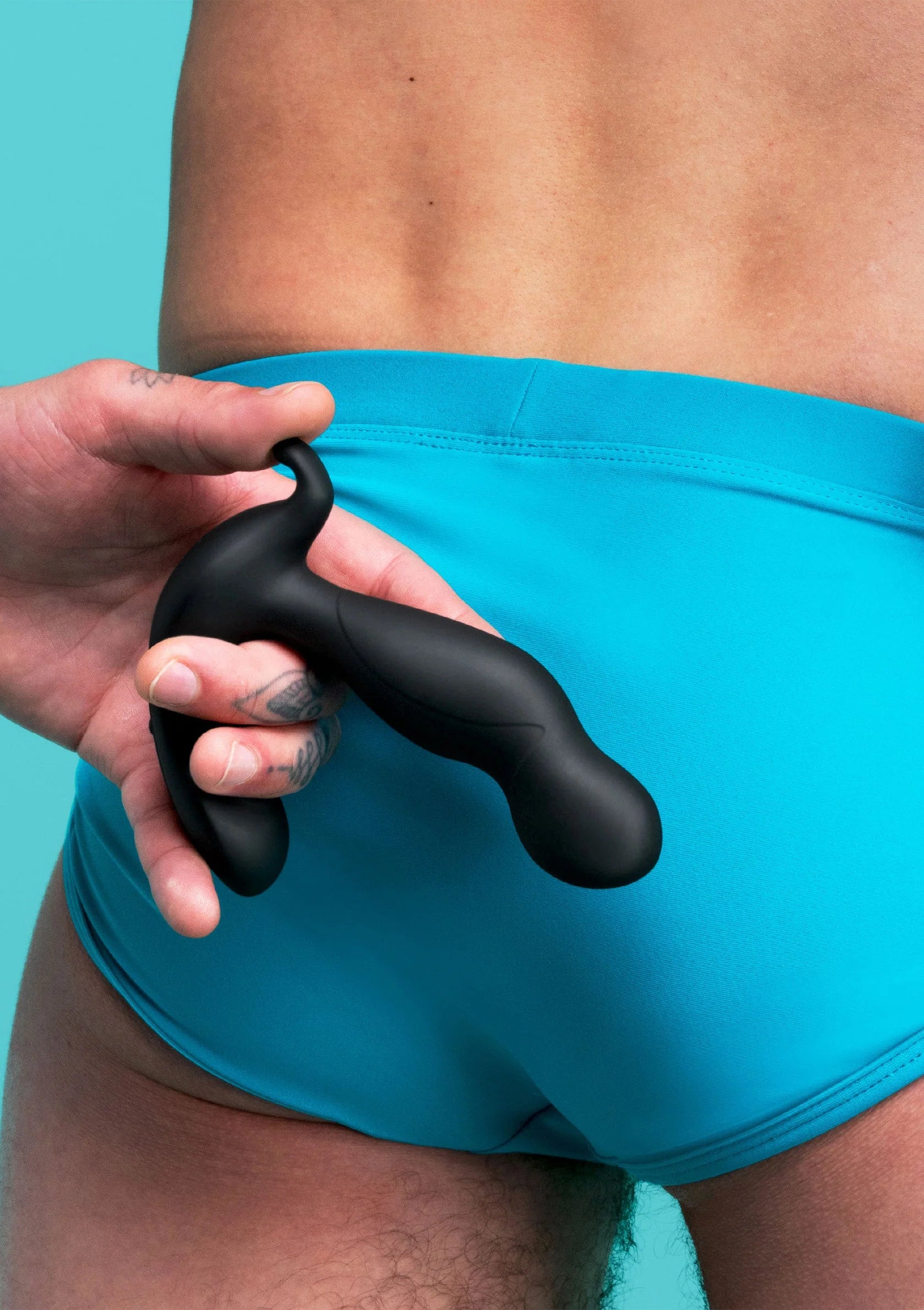 Zwarte plug van B-Vibe in hand, vlak bij turquoise short