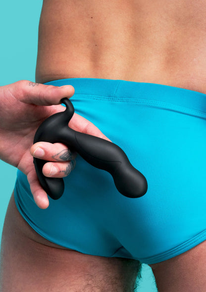 Zwarte plug van B-Vibe in hand, vlak bij turquoise short
