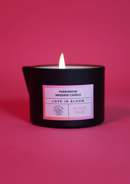 Zwarte massagekaars met etiket Love in Bloom en Sunny Daze, met brandende pit.