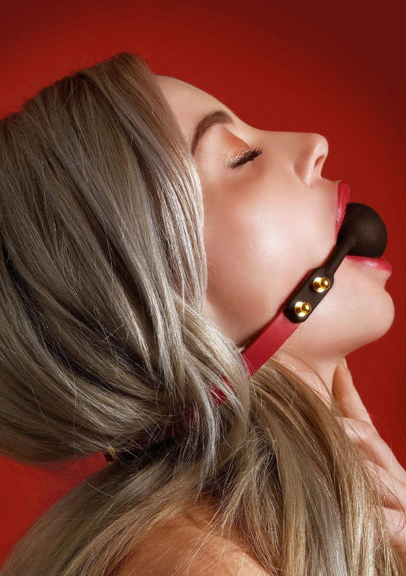 Zwarte siliconen ball-gag met rode band en gouden klinknagels op model